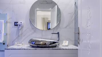A bathroom with a marble sink, a round mirror, a hairdryer, and a towel rack.