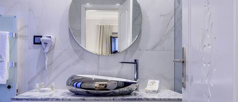 A bathroom with a marble sink, a round mirror, a hairdryer, and a towel rack.