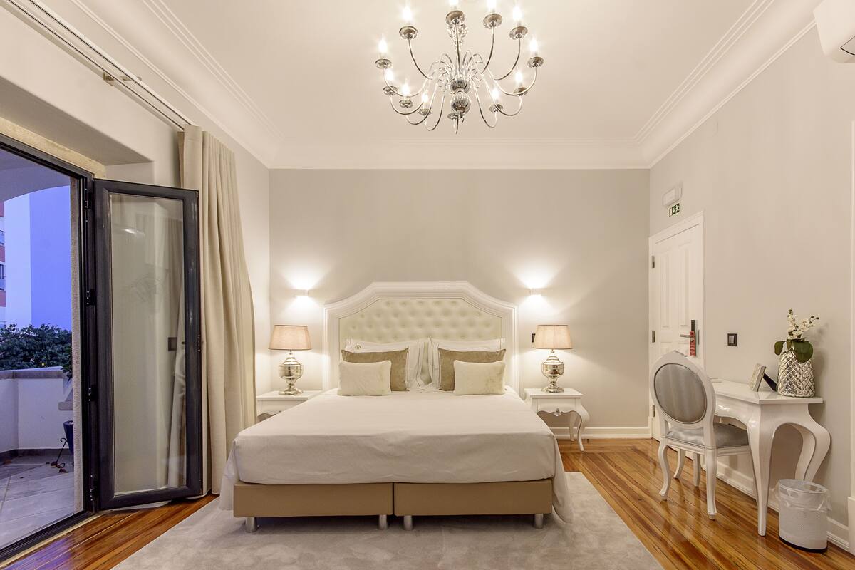 A bedroom with a large bed, a chandelier, a desk, and a chair.