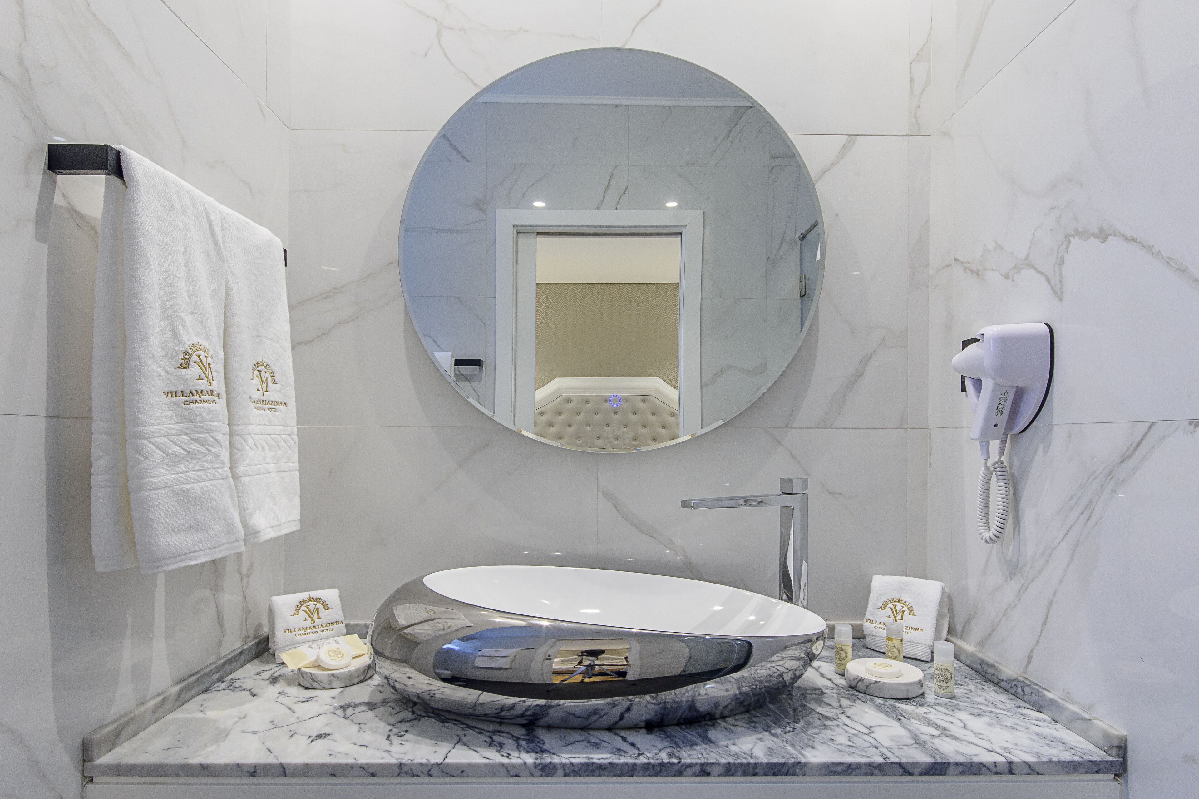 A modern bathroom with a round mirror, a white sink, and a hairdryer on the wall.