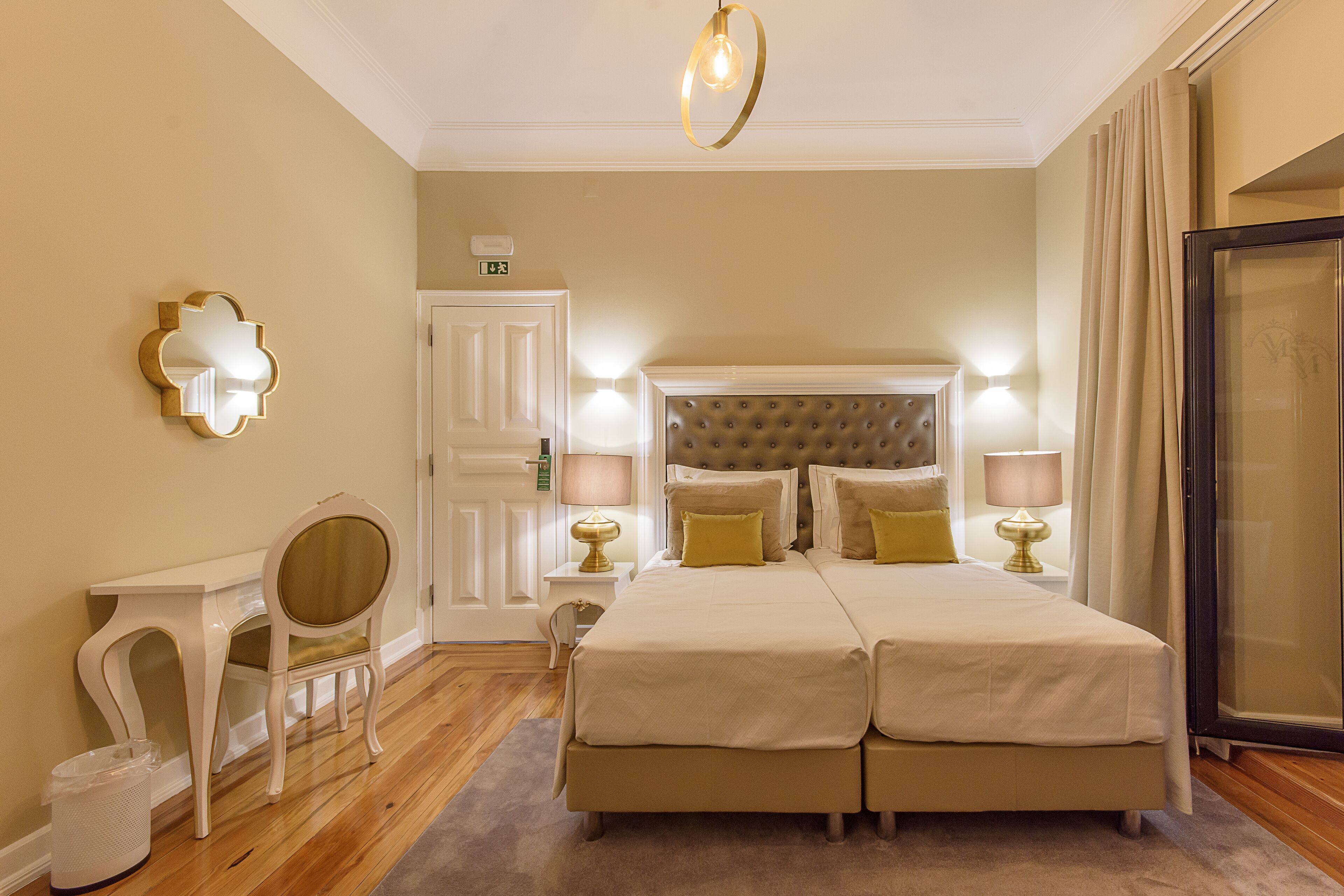 A hotel room with a large bed, bedside lamps, a chair, a small table, and a mirror on the wall.