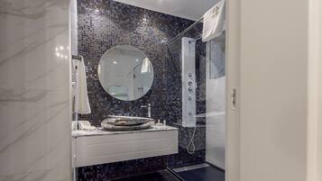 Un baño moderno con tocador de mármol, espejo redondo, cabina de ducha de vidrio y salpicadero de mosaicos.