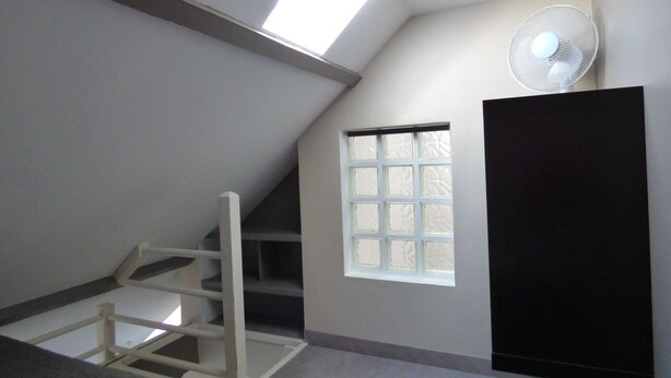 A sloped ceiling with a skylight, a window, and a standing fan. - Appartement n°8 au 3ème Étage Sans Ascenseur (Berck-sur-mer)
