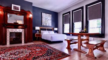 A bedroom with a large bed, a wooden table, a fireplace, and a large window.