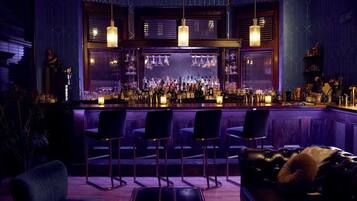 A bar area with multiple bar stools, a counter with bottles, and hanging pendant lights.