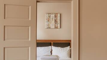 Quarto de hotel com piso de madeira, cama com roupa de cama branca e uma obra de arte na parede.