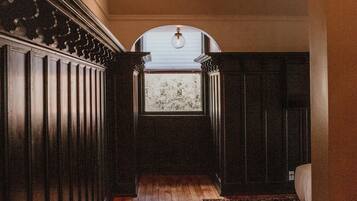 A hallway with wooden flooring, a dark wooden paneling on the left, and a patterned rug on the right.