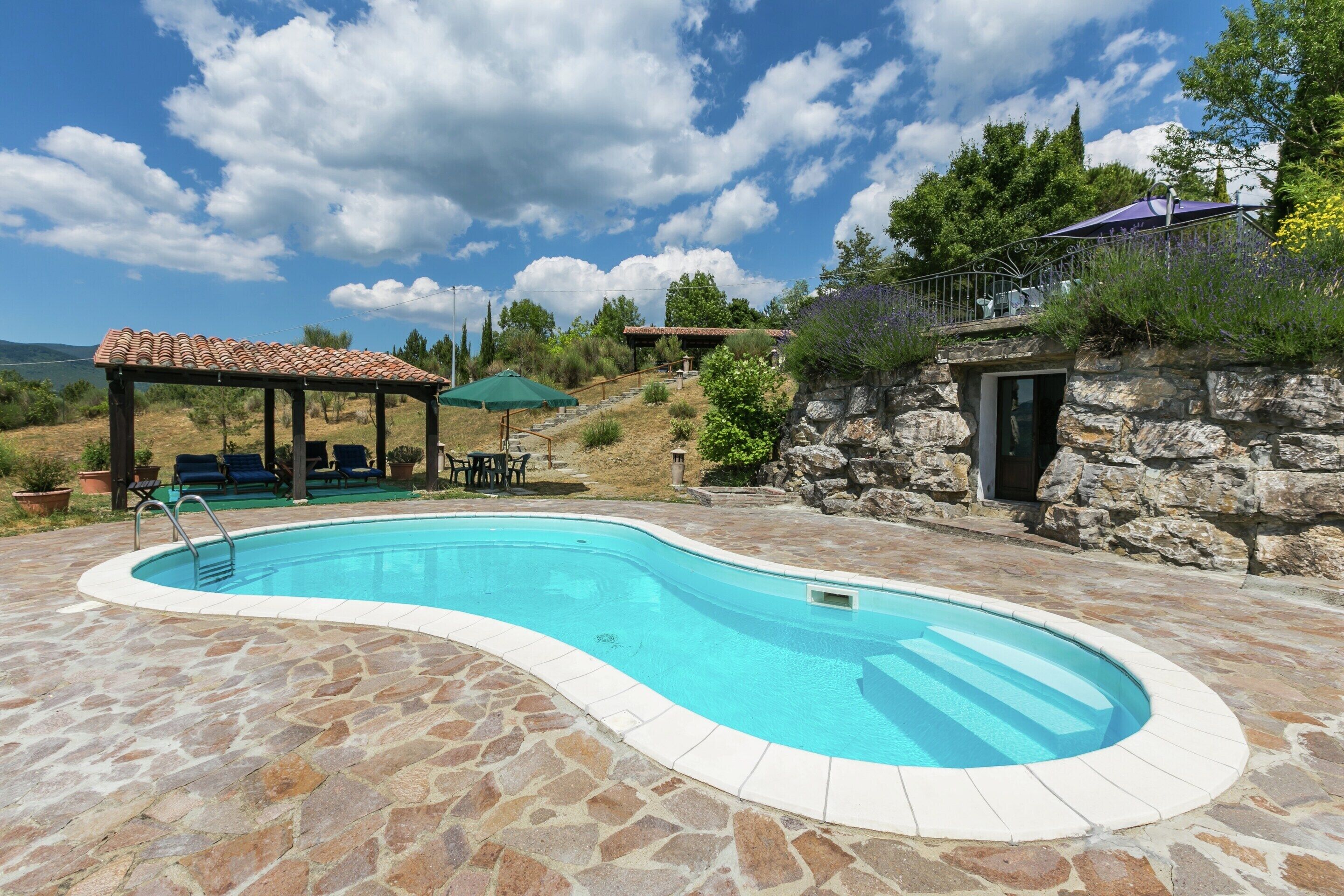 A swimming pool with stone tiles, a covered seating area, and a stone wall.