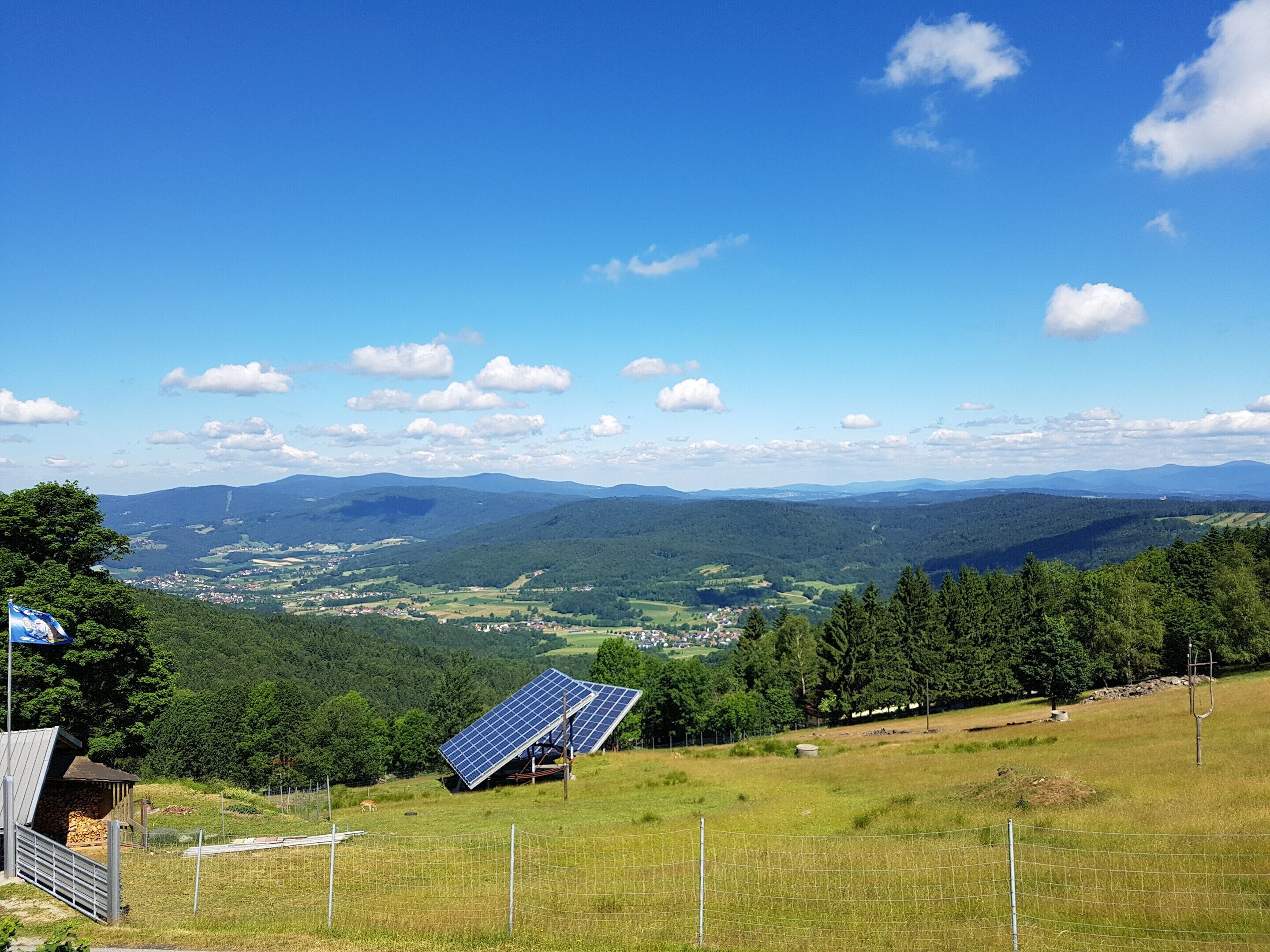 A rural landscape with a solar panel installation, a stone building, and a fenced area.