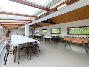 A spacious indoor area with multiple tables and chairs, a foosball table, and large windows allowing natural light.