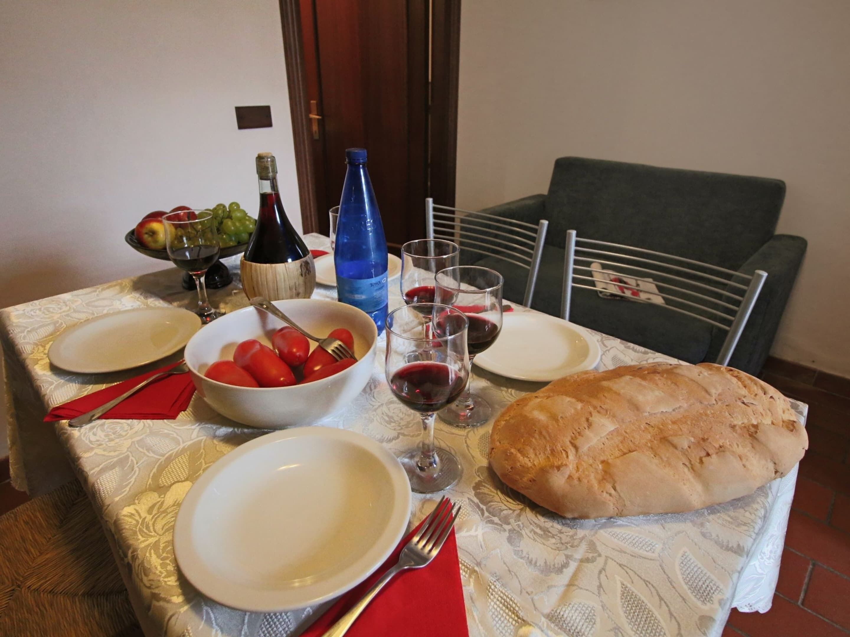 A dining table set with plates, bowls, glasses, a bottle, and a loaf of bread.