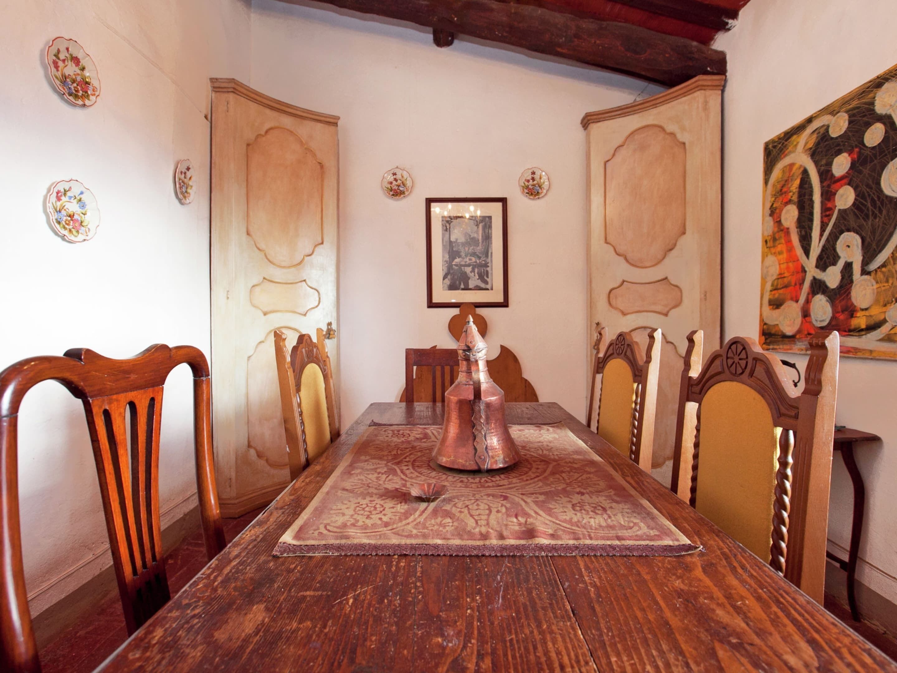 Ein Esszimmer mit Holztisch, Stühlen, einem gemusterten Teppich und dekorativen Tellern an den Wänden.