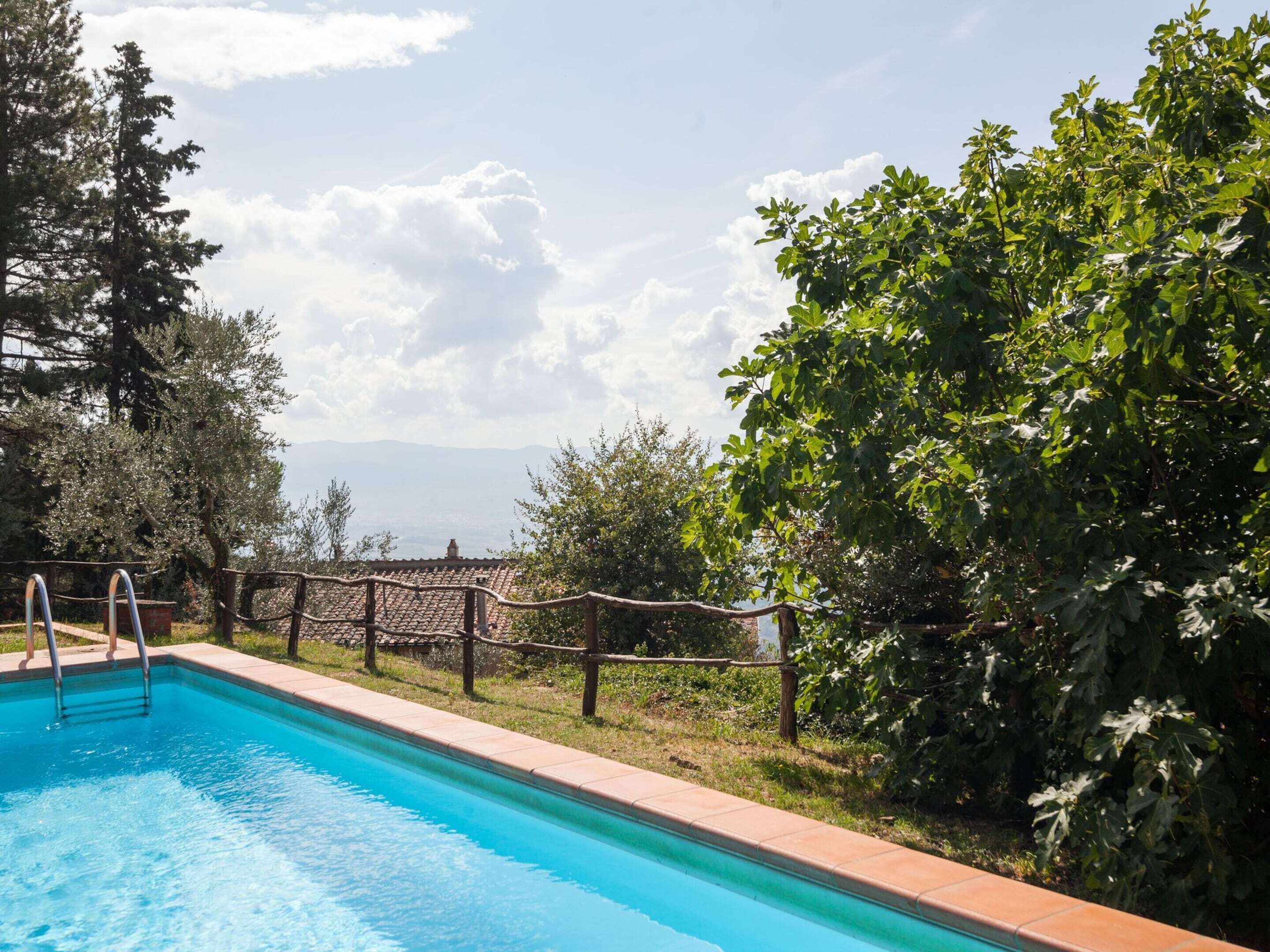 A swimming pool with a wooden fence, surrounded by trees and a view of distant buildings.