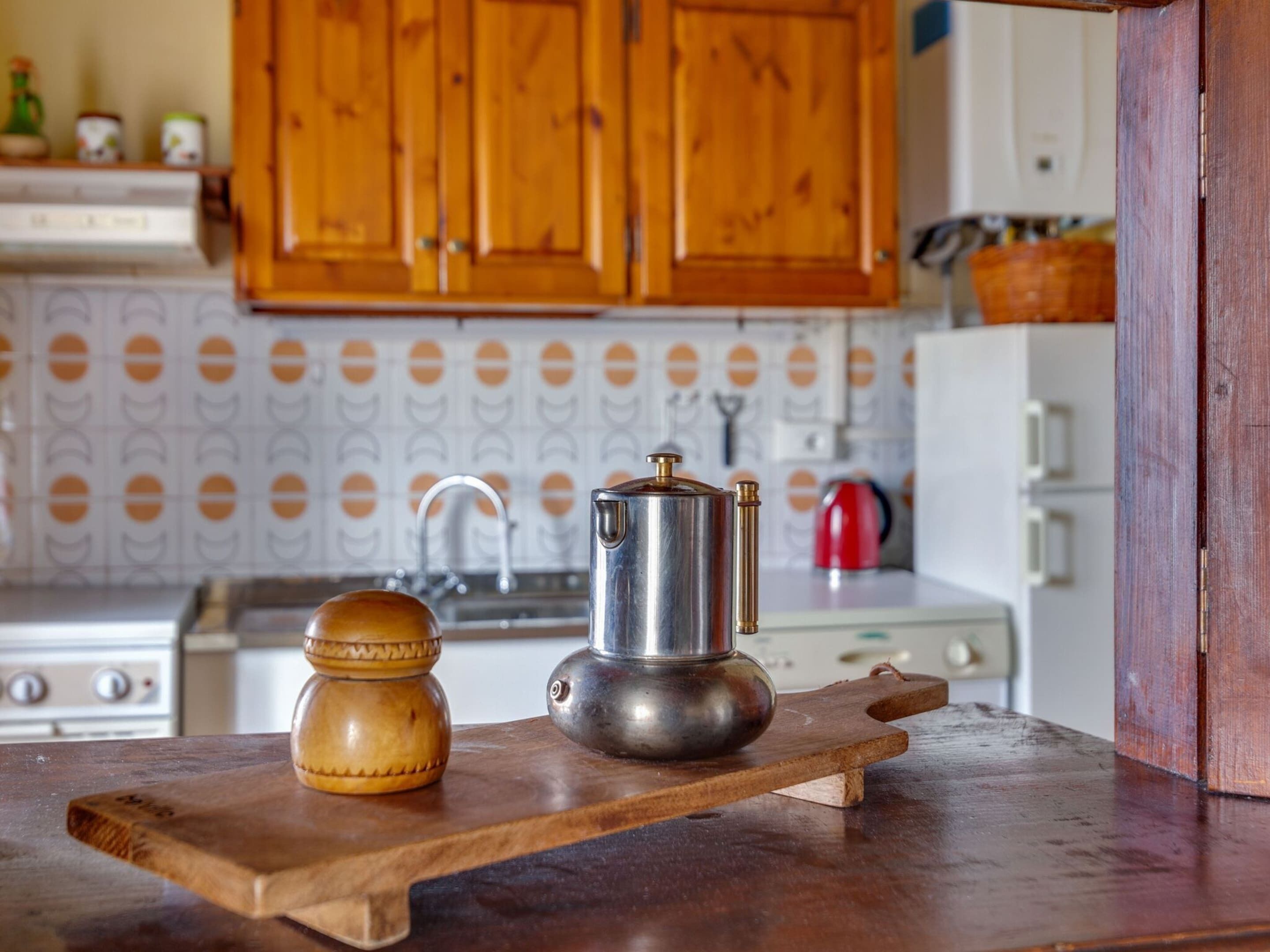 A kitchen with wooden cabinets, a stainless steel coffee pot, and a wooden spice jar on a cutting board.