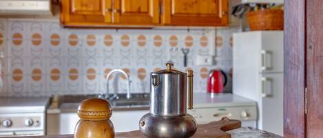 A kitchen with wooden cabinets, a stainless steel coffee pot, and a wooden spice jar on a cutting board.