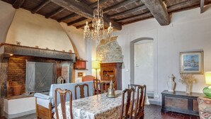 A rustic dining room with a stone fireplace, wooden beams, and a chandelier. - Apartment Tuscany Near Pratomagno Mountain (Castelfranco Piandisco)