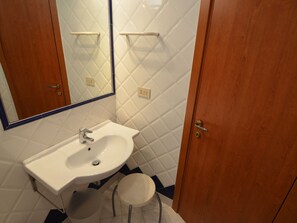 Une salle de bain avec un lavabo blanc, un miroir et une porte en bois.