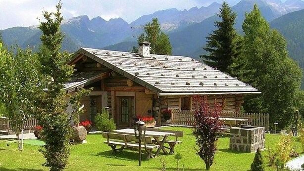 A log cabin with a sloped roof, surrounded by a well-maintained lawn and a wooden fence.