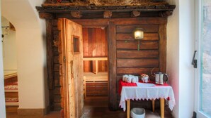 A rustic wooden room with a wooden bench, a table with a white tablecloth, and a window.