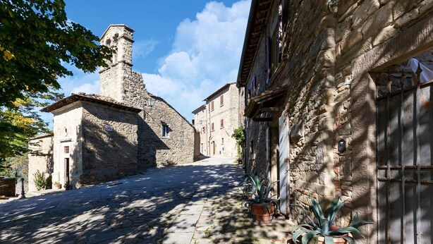 Eine schmale Kopfsteinpflasterstraße, gesäumt von Steinhäusern mit traditioneller Architektur, darunter ein markanter Turm.