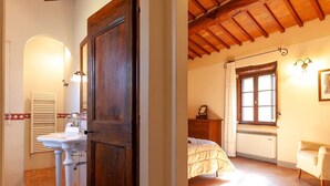 Ein Schlafzimmer mit einem Bett, einem Nachttisch, einem Fenster und einem Sessel.
