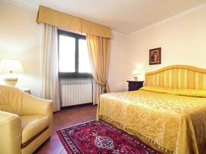 Ein Hotelzimmer mit einem Bett, einem Sessel, einem Fenster mit Vorhängen, einer Heizung und einer Lampe.