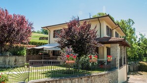 A two-story house with a stone facade, a balcony, and a garden with red flowers. - Villa in Lonnano With Pool (Pratovecchio Stia)