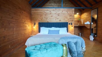 Un dormitorio de cabaña de madera con una cama, un banco tapizado azul y una mesita de noche pequeña.