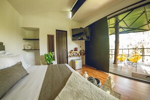 Un dormitorio moderno con una cama grande, un televisor, un escritorio pequeño y un balcón con sillas amarillas.