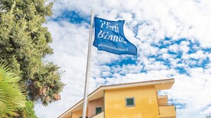 A flag with "Il Marti Bianu" and a website URL, a yellow building with balconies, and a clear sky with clouds. - Holiday Home in Gallura Near White Sandy Beach (Santa Teresa di Gallura)