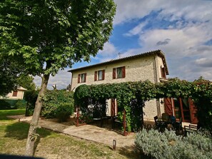 Un edificio in pietra con giardino, una pergola e sedute all'aperto.