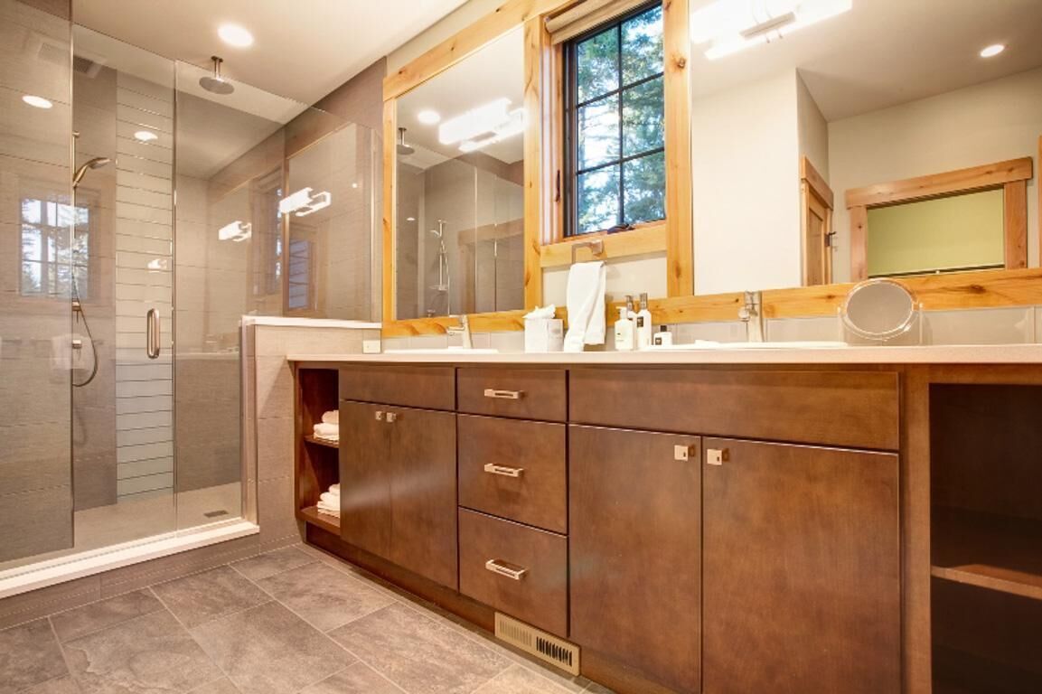 A bathroom with a glass-enclosed shower, wooden vanity with drawers, and a large mirror above the sink.