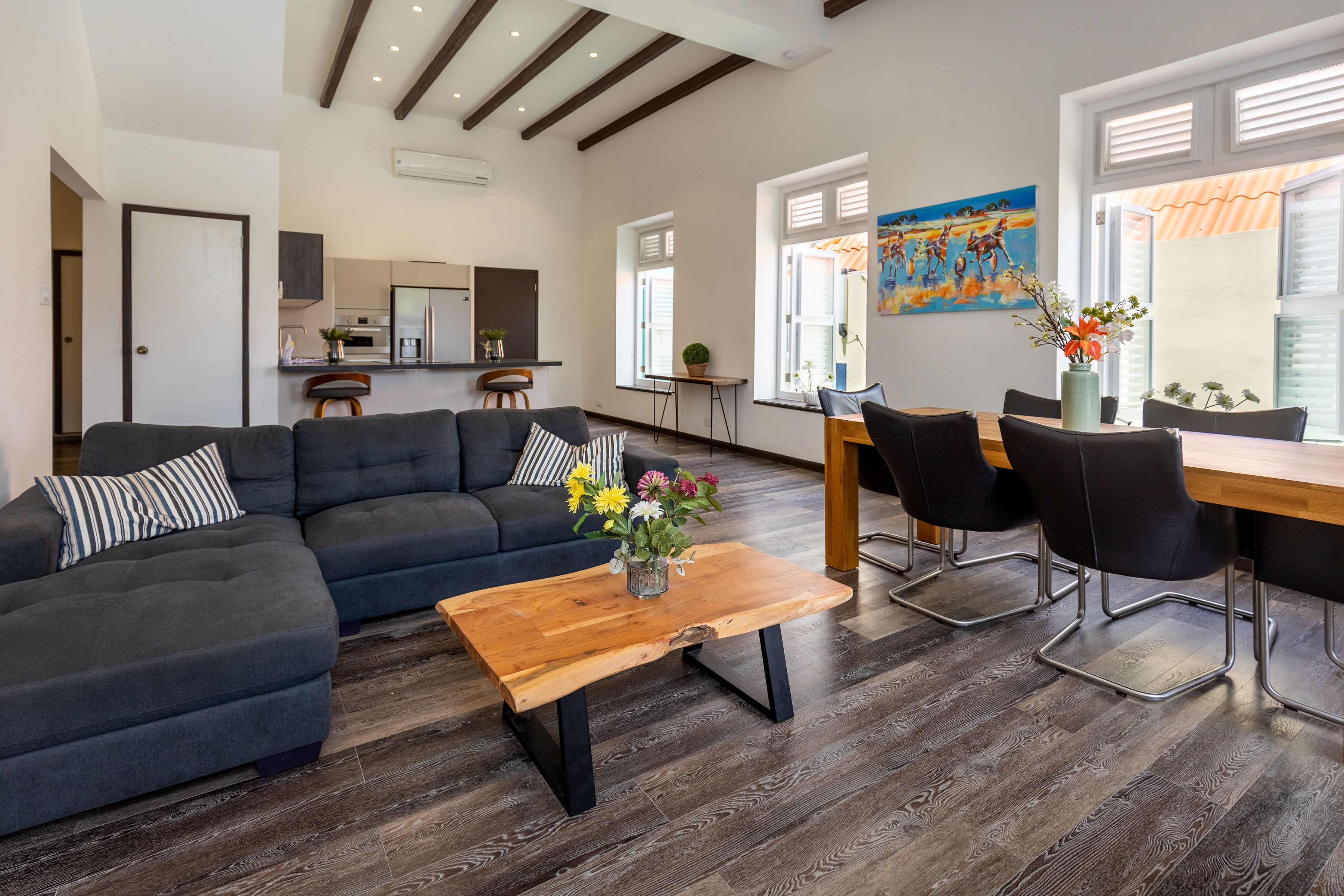A modern living room with a sectional sofa, a wooden coffee table, and a dining area with chairs and a table.
