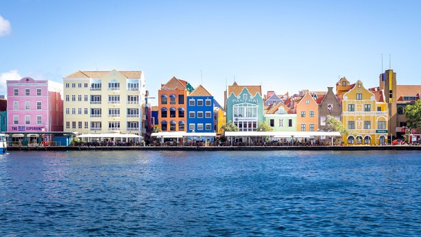 A waterfront with colorful buildings, including a pink building with a sign that reads "The Blue Experience." - Private City Centre Apartment Located at Famous Handelskade (Willemstad)