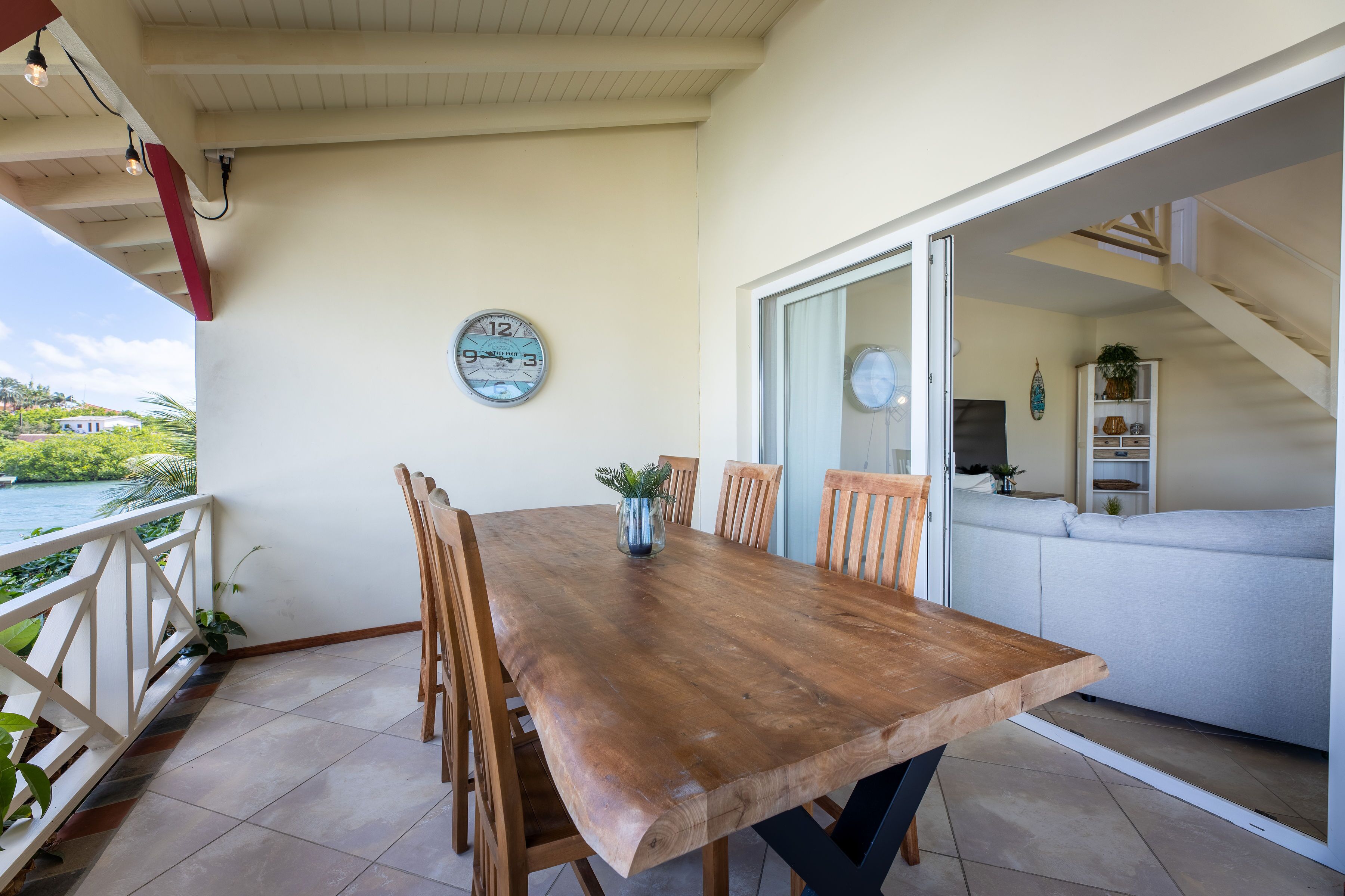 Una mesa de madera con sillas, un reloj y vista al mar.