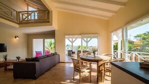 A spacious living area with a high ceiling, a dining table with chairs, a sofa, and a TV mounted on the wall. - Spanish Water Marina Apartments (Jan Thiel)