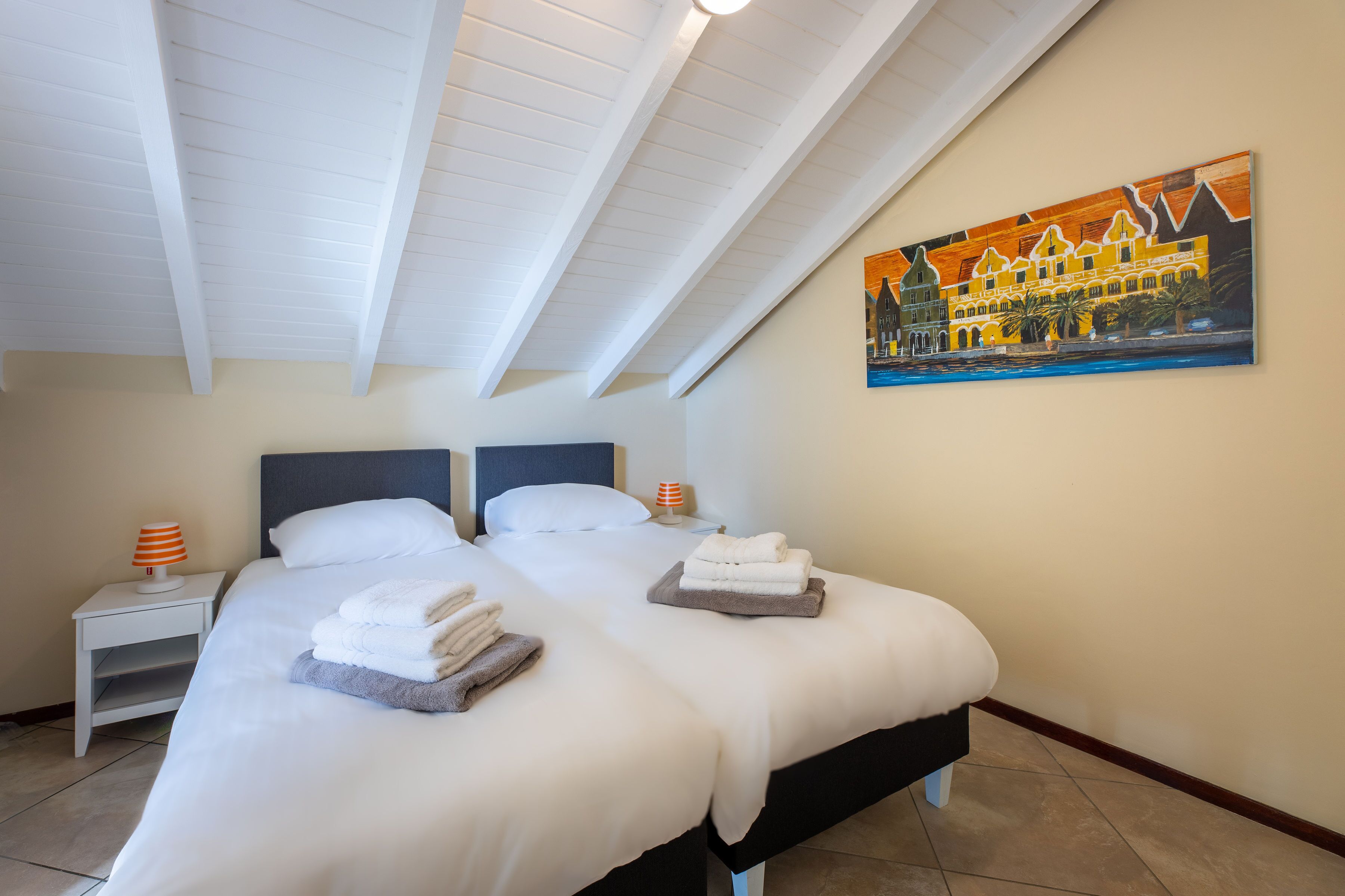Een hotelkamer met twee bedden, witte lakens, een schilderij aan de muur en een schuine plafond.