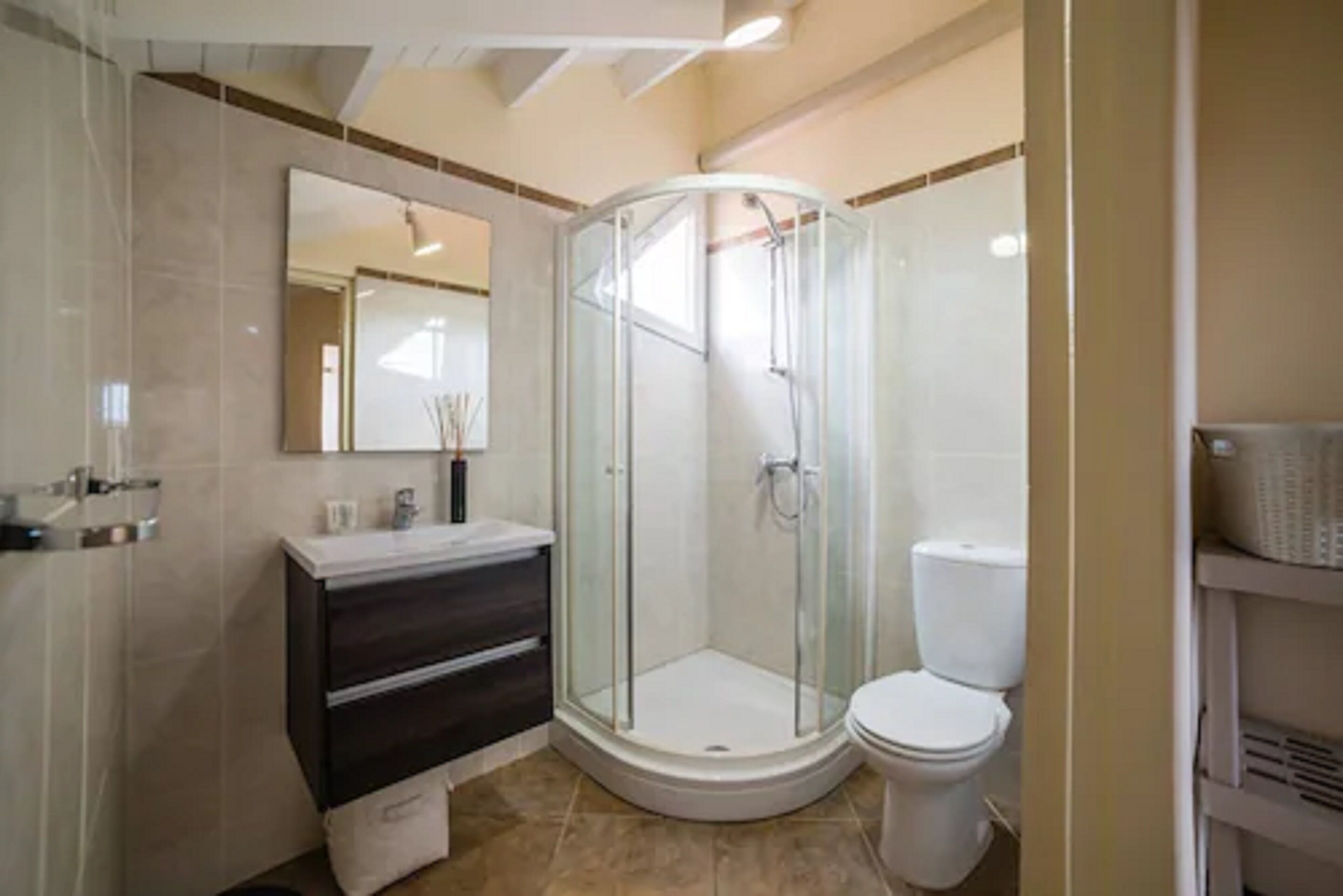 Un baño moderno con ducha envuelta en vidrio, inodoro blanco y tocador oscuro.