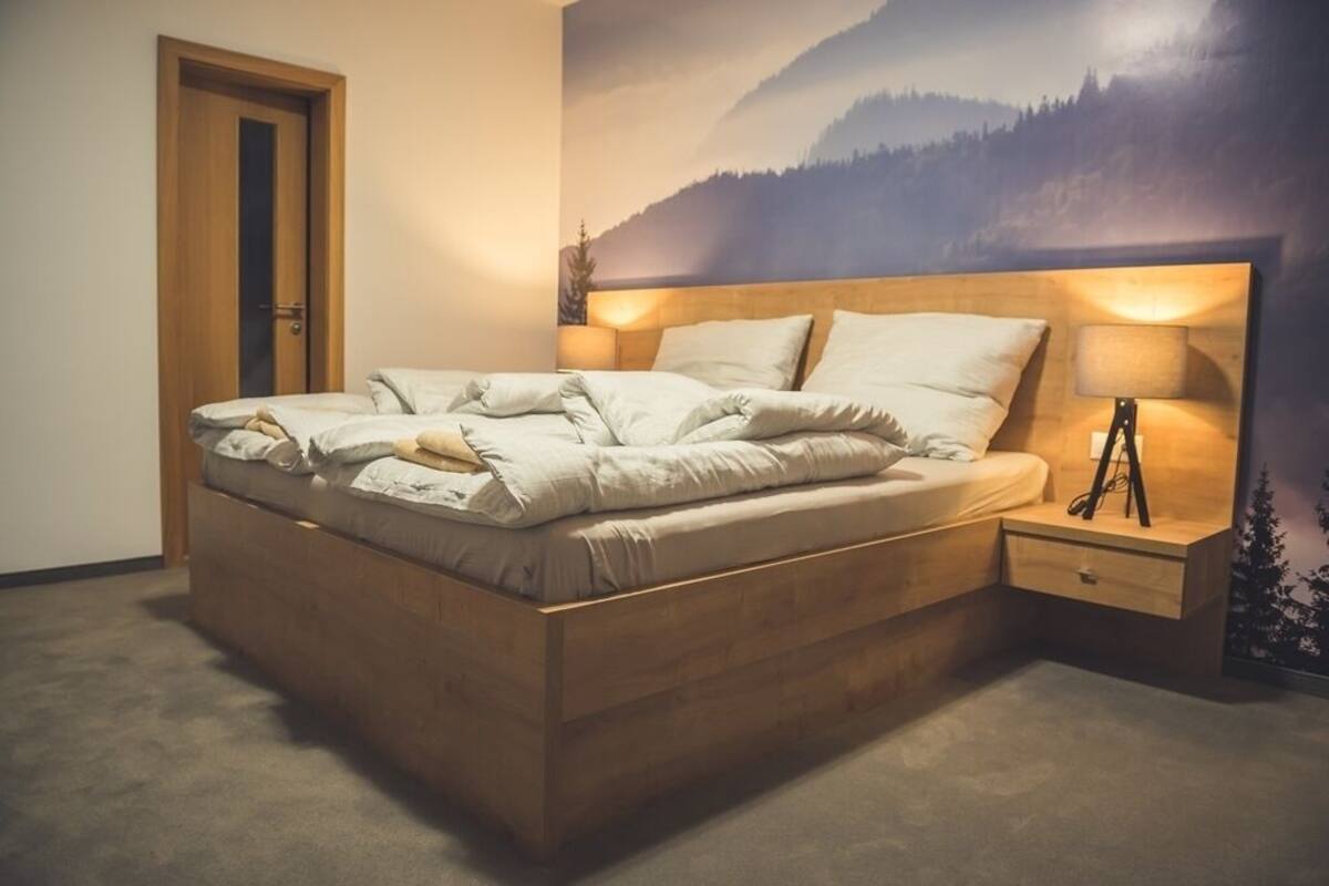 Quarto com cama de madeira, mesa de cabeceira e um mural na parede com paisagem de montanhas.