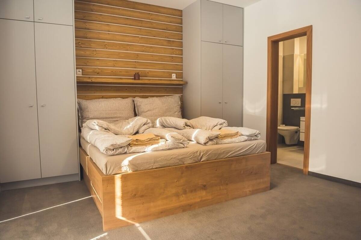 Quarto com estrutura de cama de madeira, painel de cabeceira fixo e guarda-roupa com portas de correr.