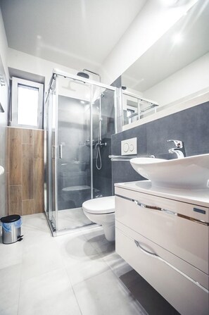 Un baño moderno con ducha acristalada, un lavamanos blanco y suelo de madera.
