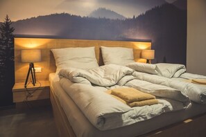 Una cama con cabecera de madera, dos lámparas de noche y un paisaje de montaña al fondo.