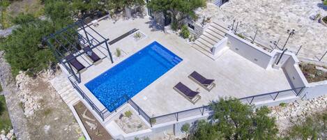 Vue aérienne d’une propriété dotée d’une piscine, de bâtiments en pierre et d’un environnement verdoyant.