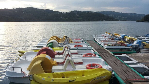 A row of colorful inflatable boats docked at a pier with a calm lake and hills in the background. - Peaceful Stay With Garden (Alto Reno Terme)