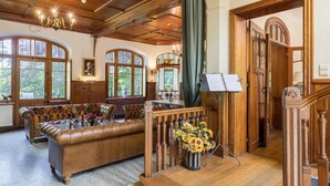 A spacious room with a leather sofa, wooden flooring, large windows, and a chandelier. - Beautiful Castle in Spa wit Garden (Spa)