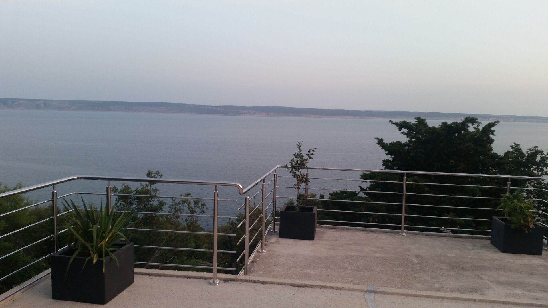 A balcony with a metal railing overlooking a body of water. There are potted plants on the balcony.