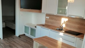 Een moderne keuken met witte kasten, een houten aanrechtblad, een ingebouwde oven en een tv boven het aanrecht. Er staan twee witte barkrukken met chromen poten.