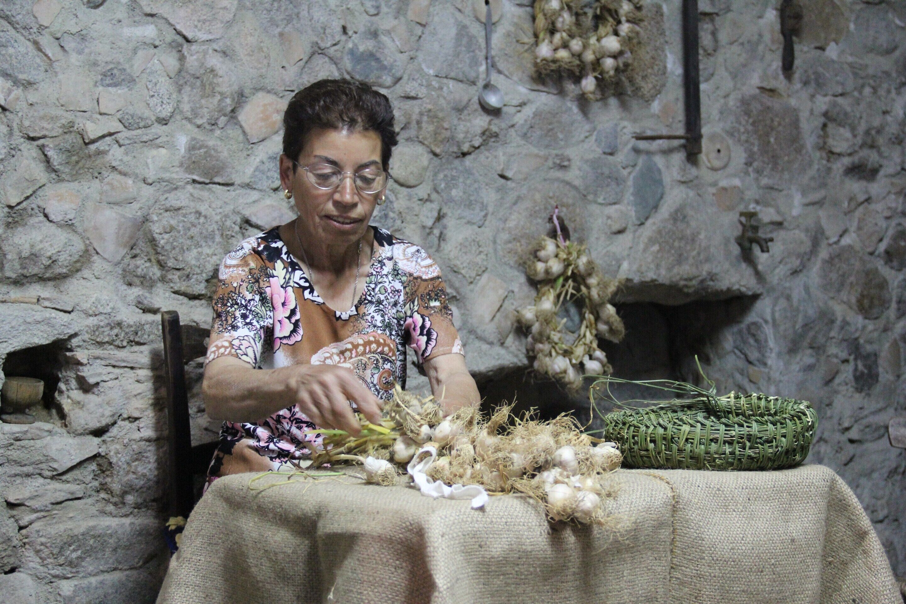 A person sitting at a table with a woven basket and garlic bulbs.