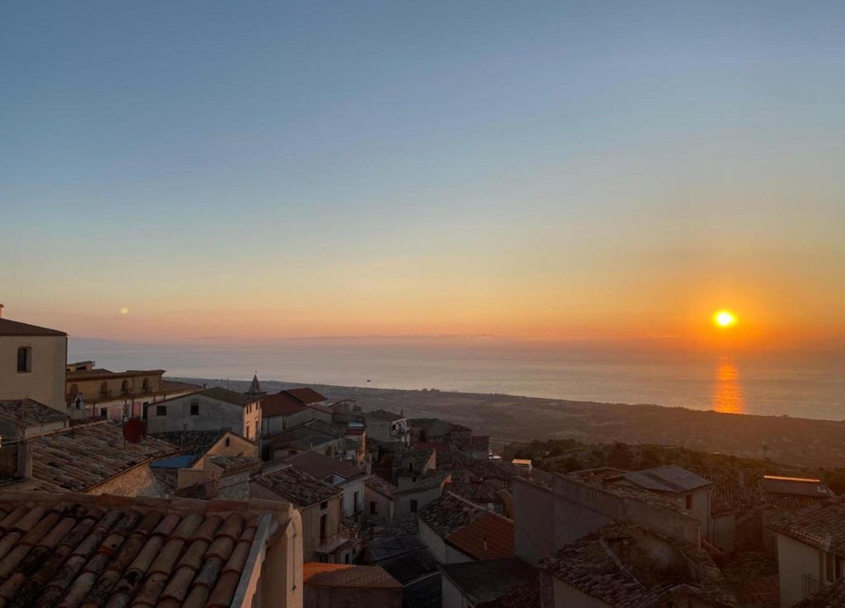 A coastal town at sunset with buildings and a clear view of the sea.
