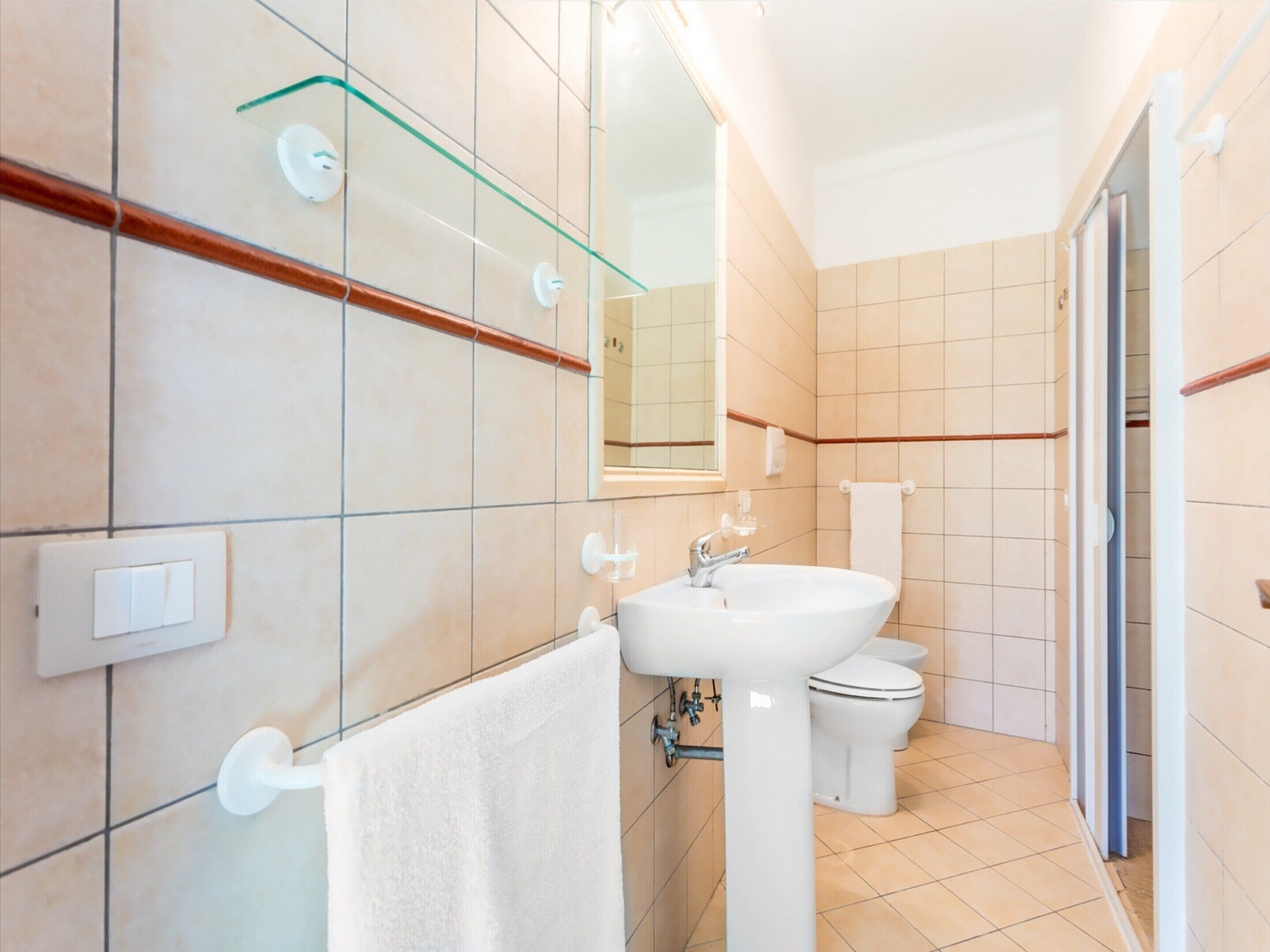 A modern bathroom with a white sink, toilet, and glass shower enclosure.